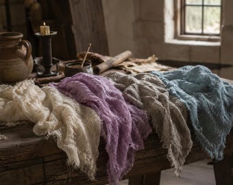 May include: A collection of four rectangular fabric runners in cream, lavender, beige, and light blue. Each runner features a loose, open-weave texture with frayed, unfinished edges, draped across a wooden surface in a layered arrangement.