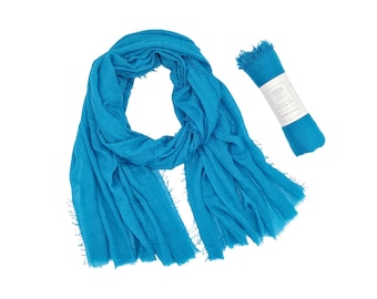 May include: A turquoise blue cotton scarf with frayed edges. The scarf is folded and rolled up, with a white label attached.