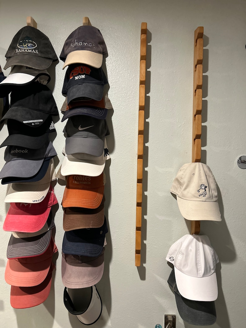 May include: A wall mounted hat rack with two wooden rails. The rails are filled with a variety of baseball caps in different colors and designs. The caps include brands like "Life is Good", "Trobbies California", "Bahamas", and "Surf Mom".
