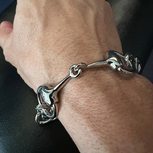 May include: A silver bracelet featuring a horse bit design. The bracelet is made of metal and has a polished finish.