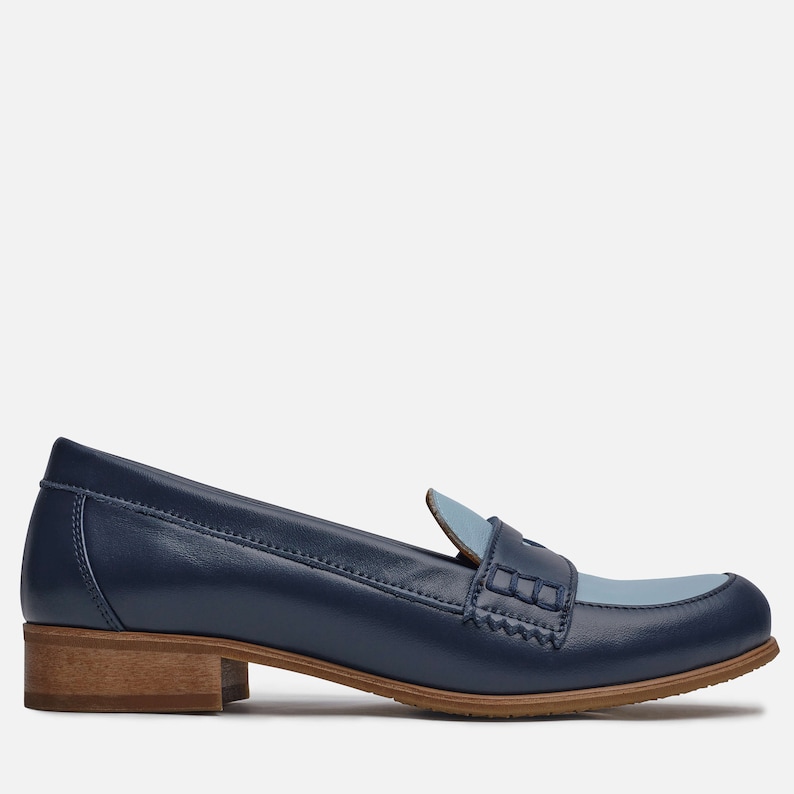 May include: A pair of blue leather loafers with a light blue leather accent on the toe. The loafers have a brown wooden heel.