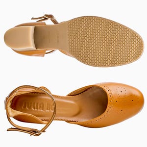 Puede incluir: Dos pares de zapatos de cuero color marr&oacute;n claro con correas en el tobillo y tacones peque&ntilde;os. Los zapatos tienen un dise&ntilde;o cl&aacute;sico con perforaciones decorativas en la puntera. Las suelas son de color marr&oacute;n claro con un patr&oacute;n texturizado. La marca "JULIA BO" es visible.