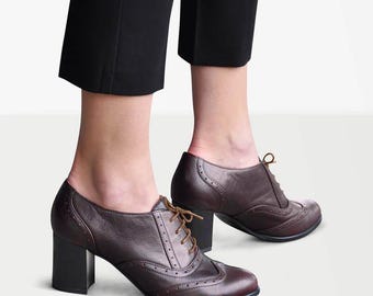 May include: Brown leather lace-up heeled shoes with a brogue design. The shoes have a chunky heel and a rounded toe.