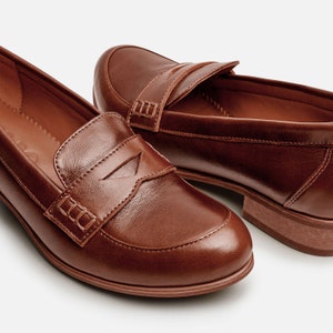 May include: A pair of brown leather loafers with a classic penny loafer design. The loafers have a slightly rounded toe and a low heel.