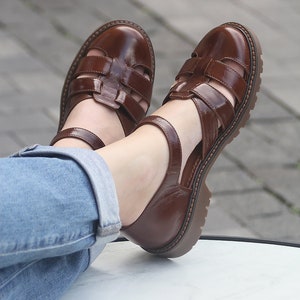 May include: Brown leather sandals with a caged design and a chunky heel. The sandals have a strap that goes around the ankle.
