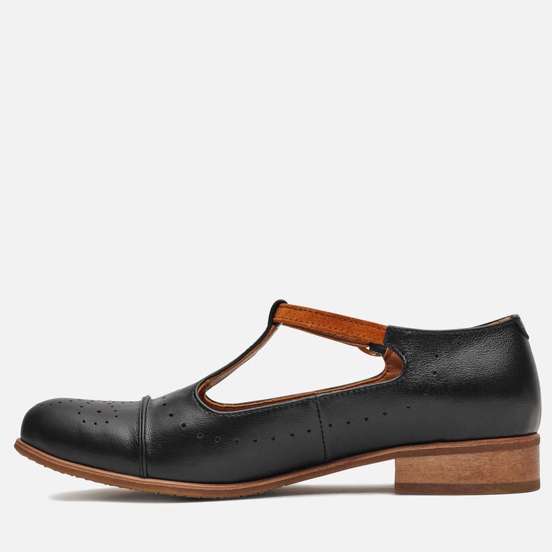 May include: Black leather t-strap shoes with a brown leather strap and a low block heel.