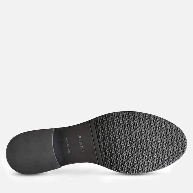 May include: Black shoe sole with a textured pattern and a smooth heel. The sole has the brand name "JULIUS" printed on it. The shoe sole is made of a durable material.