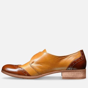 May include: A brown and tan leather women's shoe with a buckle strap and a brogue design.