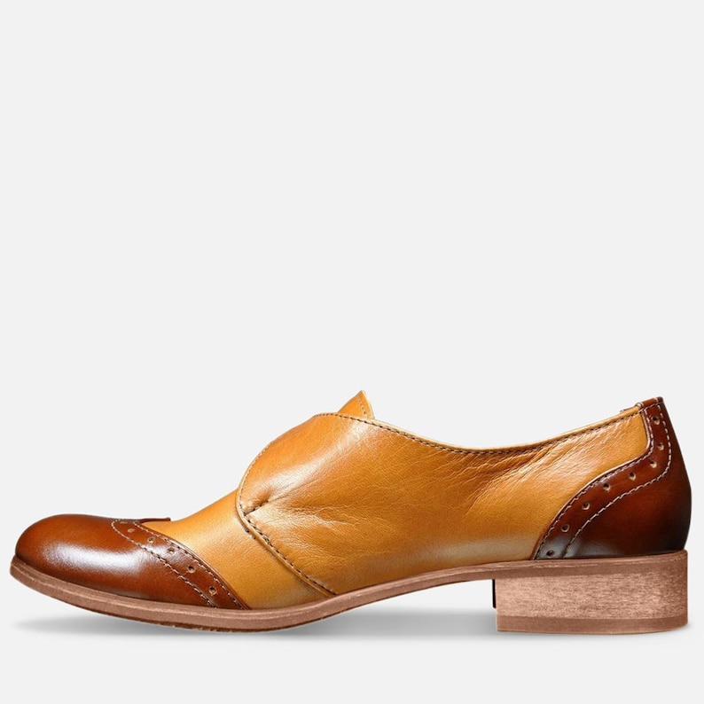 May include: A brown and tan leather women's shoe with a buckle strap and a brogue design.