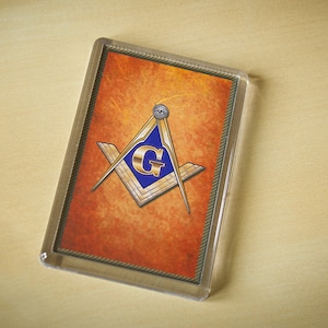 May include: A gold and blue Masonic compass and square with an all-seeing eye on a textured orange background.