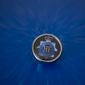 May include: A silver and blue badge with the text "Banford Police" and the letters "HF" in the centre.
