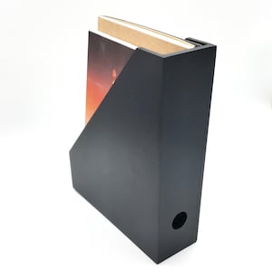 Può includere: Cartella porta riviste nera con un libro all'interno. La cartella ha un foro sul lato per un facile accesso.