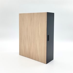 Op de afbeelding: Een houten doos met een zwart voorpaneel. De doos heeft een licht houtnerfpatroon en een zwart slot.