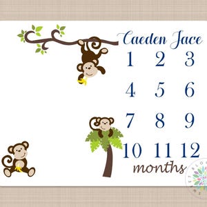 May include: A white baby milestone card with a jungle theme. It features a monkey hanging from a vine, a monkey sitting on a palm tree, and numbers 1 through 12. The text "Caeden Jace" and "months" are printed on the card.