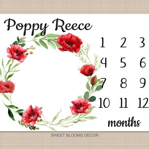 May include: A white baby milestone card with a red poppy floral wreath and the name "Poppy Reece" at the top. The card has numbers 1 through 12 for each month of the baby's first year.