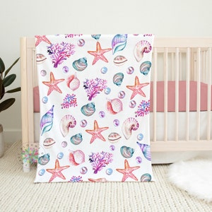 May include: A white baby blanket with a repeating pattern of pink and purple seashells, coral, and starfish.