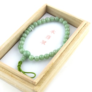 May include: A green jade prayer bead necklace in a wooden box. The box has a white label with the text "末  経" in red.