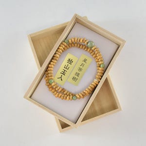 May include: A wooden box containing a brown and green beaded necklace. The box has a label that reads "星月菩提" and "猫耳人".