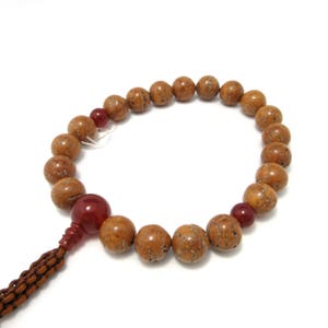 May include: A brown wooden prayer bead necklace with red agate beads. The necklace is made of natural materials and has a simple, elegant design.