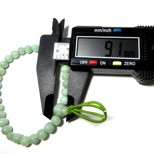 May include: A green jade bracelet with a green elastic cord closure. The bracelet is being measured with a digital caliper, which reads 9.1 mm.