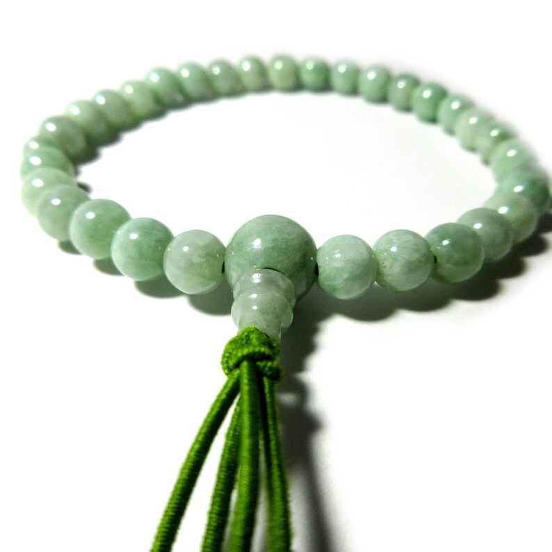 May include: A green jade prayer bead bracelet with a green tassel. The beads are round and smooth.