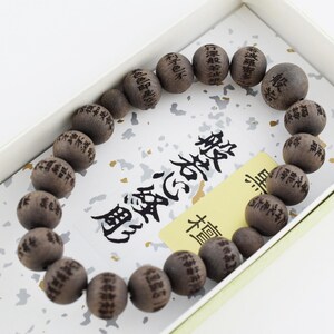 May include: A dark brown wooden bead bracelet featuring spherical beads engraved with black Chinese characters. The beads are arranged in a circular pattern, and each individual bead displays unique, intricate calligraphy text etched into the wood.