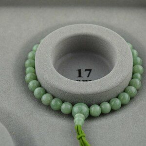 May include: A green jade bead bracelet with a tassel, displayed on a gray background. The bracelet is 17 inches long.