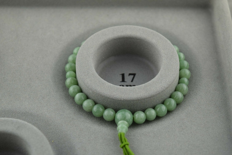 May include: A green jade bead bracelet with a tassel, displayed on a gray background. The bracelet is 17 inches long.