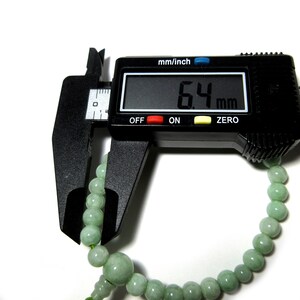 May include: A green jade bead bracelet being measured with a digital caliper. The caliper reads 6.4 mm.