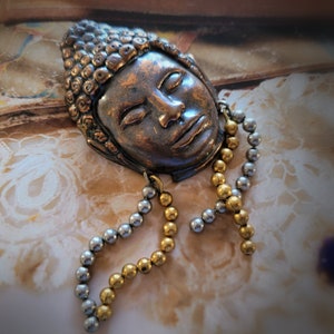 May include: A vintage bronze Buddha face brooch with a beaded chain of silver and gold beads.