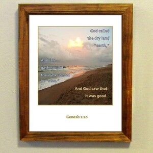 May include: A framed print with a beach scene at sunset. The print features a Bible verse from Genesis 1:10, which reads: "And the gathering of the water called he "seas." God called the dry land "earth," And God saw that it was good. Genesis 1:10"