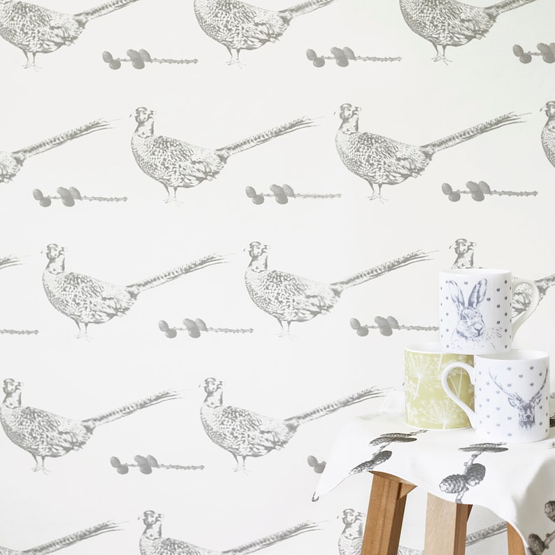 May include: White wallpaper with a repeating pattern of gray pheasants. The wallpaper is shown in a room with a wooden stool and three mugs on a white tablecloth.
