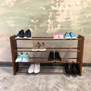 Op de afbeelding: Een houten schoenenrek met vier planken, met daarop verschillende schoenen, waaronder sneakers, sandalen en laarzen. Het rek staat op een grijs tapijt.