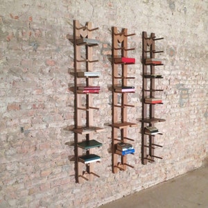 May include: Three wooden wall-mounted shelves with books on them. The shelves are made of natural wood and have a simple design. The shelves are mounted on a brick wall.