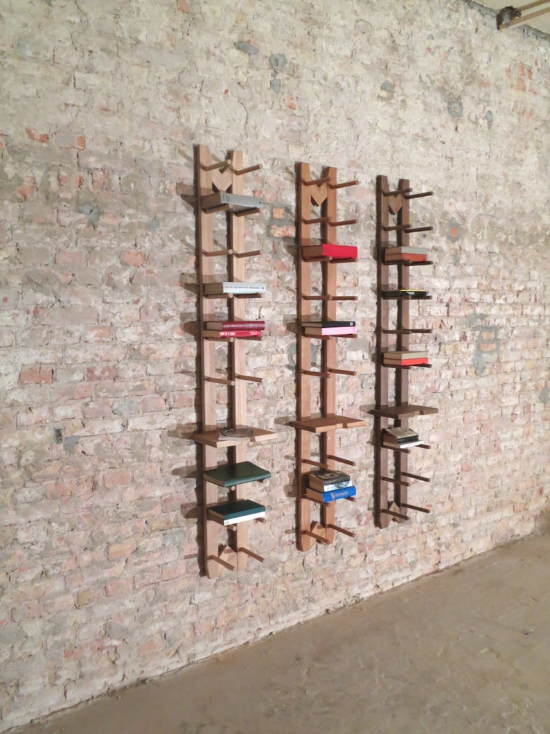 May include: Three wooden wall-mounted shelves with books on them. The shelves are made of natural wood and have a simple design. The shelves are mounted on a brick wall.