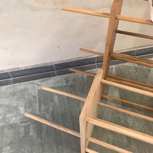 Op de afbeelding: Een houten schoenenrek met meerdere planken. Het rek is gemaakt van natuurlijk hout en heeft een rustieke uitstraling. Het rek staat op een tapijt.
