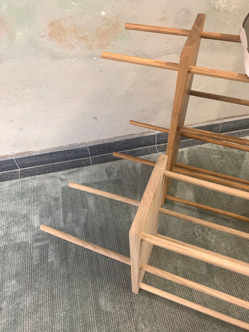 Op de afbeelding: Een houten schoenenrek met meerdere planken. Het rek is gemaakt van natuurlijk hout en heeft een rustieke uitstraling. Het rek staat op een tapijt.