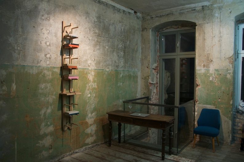 May include: A wooden shelf unit with five shelves, each holding a different colored box. The shelf unit is mounted on a wall in a room with a wooden table and a blue chair.