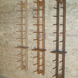 May include: Three wooden wall-mounted shelves with a unique design. Each shelf has a series of evenly spaced dowels for hanging items. The shelves are made of different shades of wood, ranging from light to dark brown.