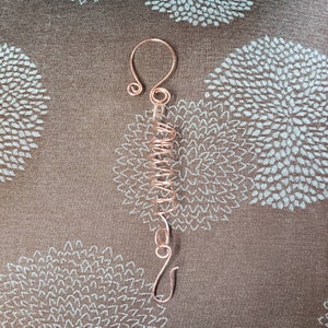 May include: A copper wire ornament with a spiral design and a hook at the bottom. The ornament is made of a single piece of wire and is a unique and decorative piece.