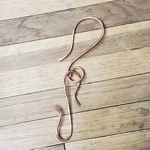 May include: A copper wire hook with a twisted design. The hook is bent into a shape that resembles a letter S.