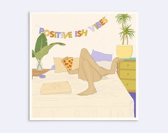 May include: A square art print featuring a person lounging on a bed with a slice of pepperoni pizza and a pizza box. A banner above reads POSITIVE ISH VIBES. The scene includes a potted plant, a nightstand, and patterned pillows in a bedroom.