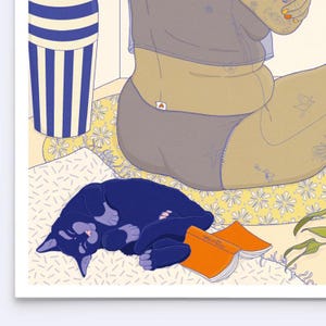May include: A black cat sleeps on a patterned cushion with an orange book titled "min-tiu". The cat is curled up with its paws tucked under its body. The cushion is covered in a yellow and white floral pattern.