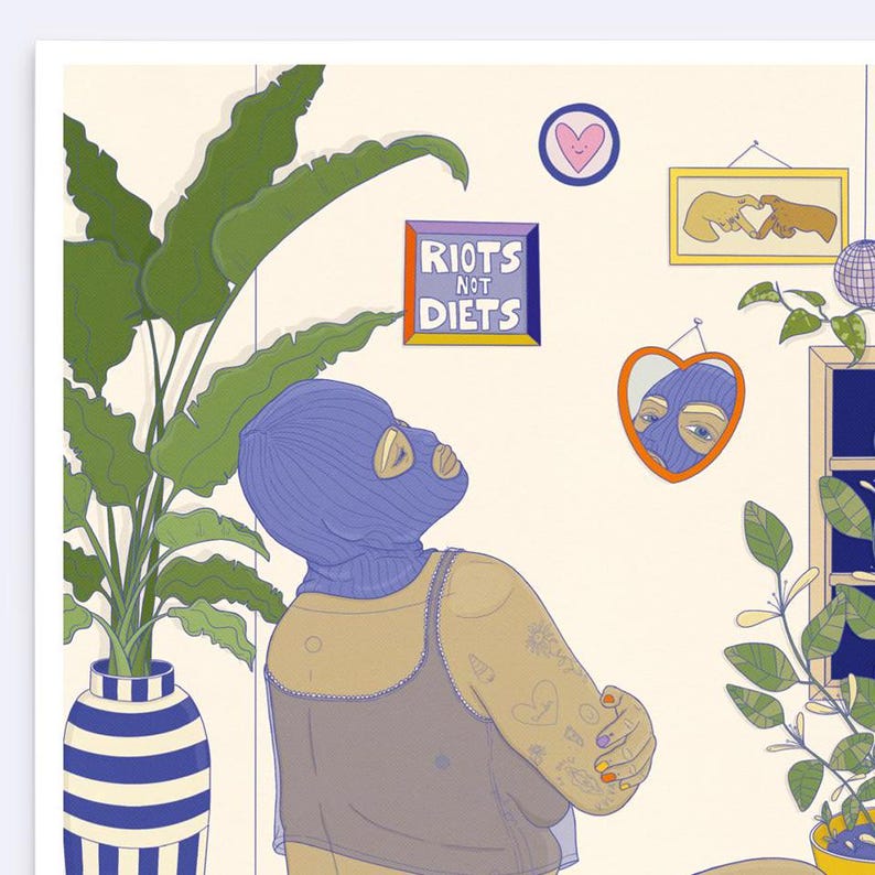 May include: A woman wearing a blue ski mask and a black tank top with tattoos on her arm. She is looking up at a sign that says "Riots Not Diets". There is a heart-shaped mirror on the wall behind her, and a plant in a blue and white striped pot in the corner.