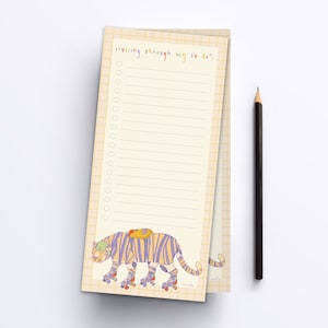 May include: A yellow and white notepad with a grid pattern on the back. The front of the notepad has a colourful illustration of a tiger wearing a backpack and roller skates. The notepad has the text "cruising through my to do's" at the top.