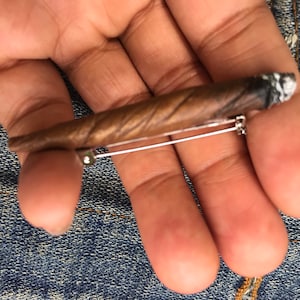 May include: A brown and black wooden cigar-shaped brooch with a silver pin and a white tip.