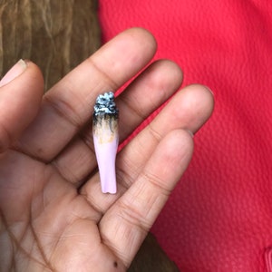 May include: A close-up of a pink and brown cigarette with the end burnt out.