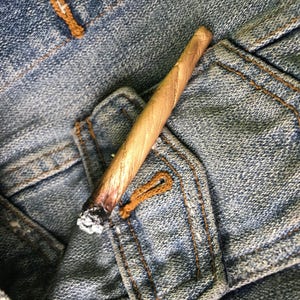 May include: A brown and white rolled cigarette on a blue denim background.