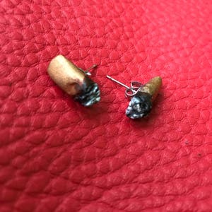 Pode incluir: Um par de brincos em forma de cigarro dourado e preto. Os brincos são feitos de metal e têm um design de cigarro realista.