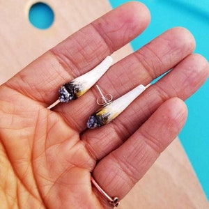 May include: A pair of small, realistic-looking cigarette earrings. The earrings are made of white clay with black and brown details to resemble a lit cigarette.